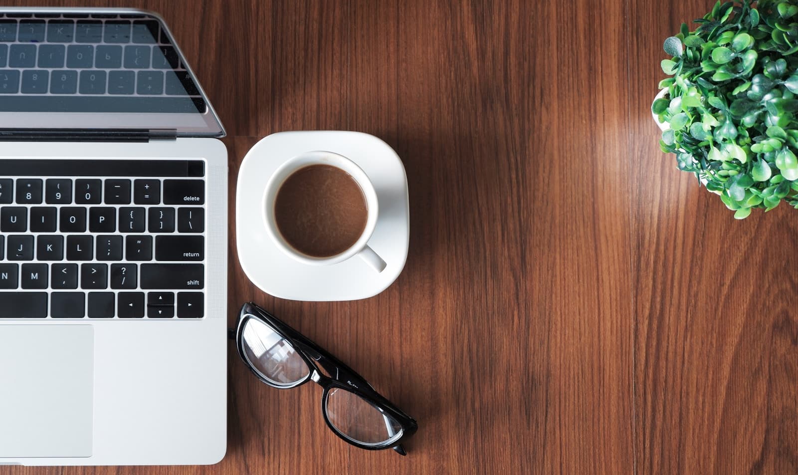 Laptop, Kaffee und eine Pflanze auf einem Holztisch als Symbol für psychologische Online-Beratung von zu Hause